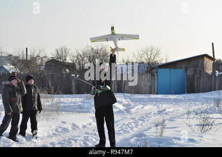Kovrov, Russia. Il 10 marzo 2012. Giovane uomo lancia la radio-controllato modello di polistirolo aereo. I bambini a camminare sulla strada guarda in corrispondenza del piano di lancio Foto Stock
