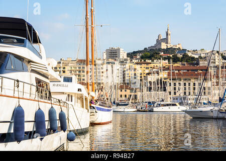 Lussuosi yacht e barche a vela ormeggiata in porto vecchio di Marsiglia, Francia, con la cattedrale di Notre Dame de la Garde basilica sulla cima della collina al tramonto. Foto Stock