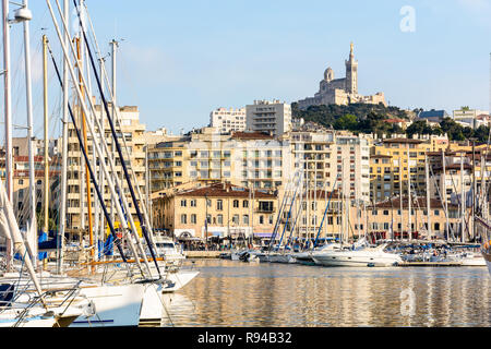 Il vecchio porto di Marsiglia, Francia, con le barche a motore e barche a vela ormeggiata in porto turistico e la Cattedrale di Notre Dame de la Garde basilica sulla cima della collina al tramonto Foto Stock