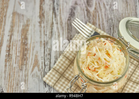 Un vasetto di crauti e carote nel proprio succo con spezie su una luce bianca, tavolo in legno, un verticale tipo di cavolo cappuccio in un vaso tradizionale home-m Foto Stock