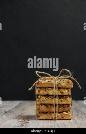 Una pila di biscotti frollini con diversi tipi di dadi a un delizioso tè o caffè al buio su un tavolo di legno. vista orizzontale. Foto Stock