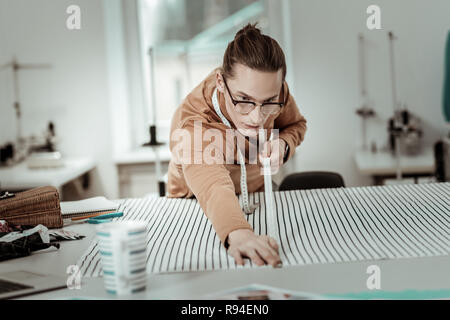 Giovani designer bello in occhiali con capelli lunghi lavora con tessili Foto Stock