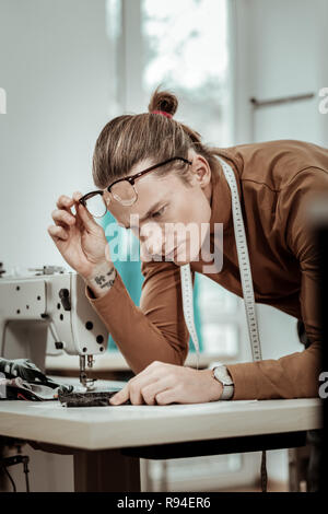 Bello con i capelli lunghi moda sarta in occhiali cercando gravi Foto Stock