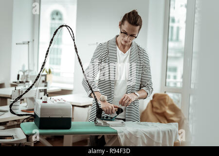 Elegante giovani designer di moda in una camicia a righe facendo servizio stireria Foto Stock