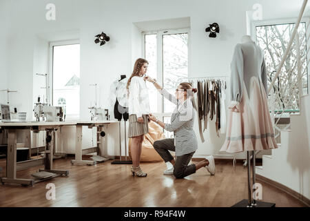 Adorabile ragazza dai capelli scuri in un mantello di colore beige a lavorare con un designer di moda Foto Stock