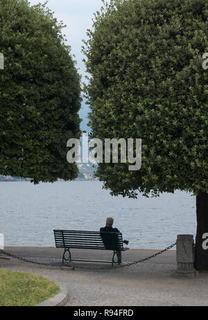 Uomo seduto su una panchina di fronte al lago di Como, Como, Italia Foto Stock