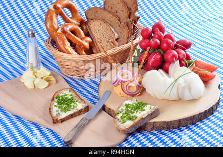 Snack bavarese con formaggio specialità chiamata 'obazda', servito con anelli di cipolla, salatini e ravanelli su un piatto di legno Foto Stock