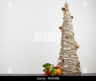 Golden decorativo albero di Natale, a forma di cono con addobbi Natale coni, giacciono accanto a orange tangerini con foglie verdi su un bianco backgrou Foto Stock