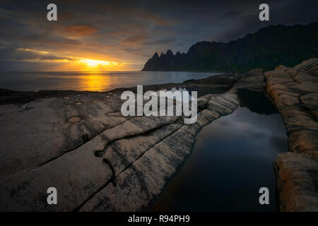 Tugeneset costa rocciosa con le montagne sullo sfondo al tramonto, Senja, Norvegia Foto Stock