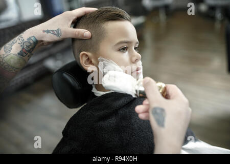 Bambini parrucchiere il taglio di Little Boy contro uno sfondo scuro. Contenti carino preschooler boy ottenere il taglio di capelli. Foto Stock