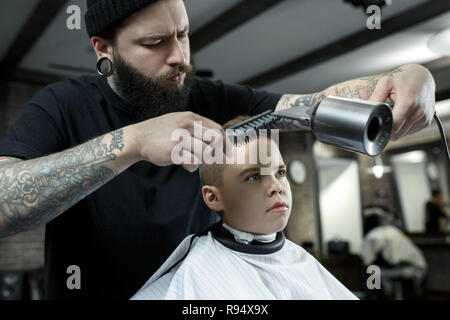 Bambini parrucchiere il taglio di Little Boy contro uno sfondo scuro. Contenti carino preschooler boy ottenere il taglio di capelli. Foto Stock