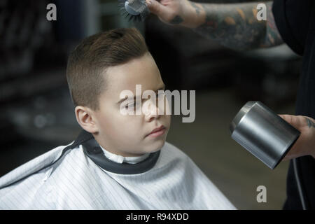 Bambini parrucchiere il taglio di Little Boy contro uno sfondo scuro. Contenti carino preschooler boy ottenere il taglio di capelli. Foto Stock