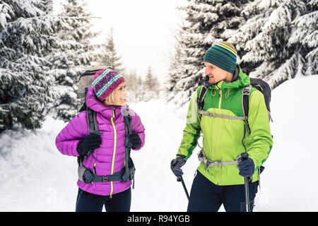 L uomo e la donna felice coppia escursionisti trekking in bianco inverno boschi e montagne. Giovani escursionismo team, la gente che camminava sul sentiero di neve con zaini, avvento Foto Stock