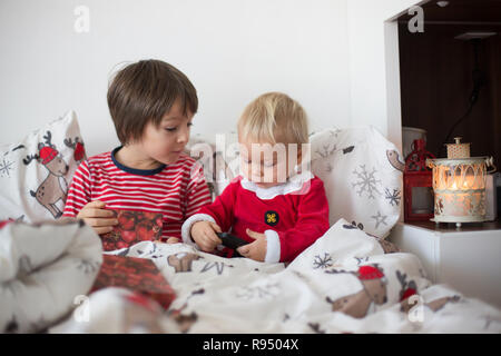 Dei bambini felici, aprendo i regali di Natale nel letto la mattina di natale Foto Stock