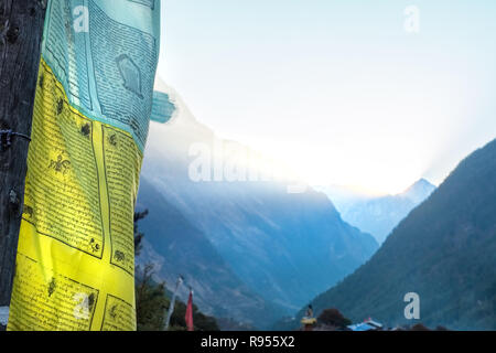 Alba nella regione di Manaslu del Nepal Himalaya con la luce del sole streaming su un crinale e bandiere di preghiera in primo piano Foto Stock