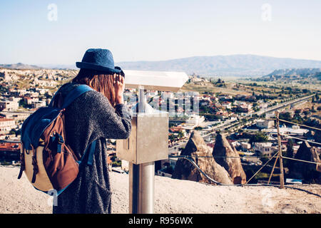 Un viaggiatore con lo zaino a viewpoint guarda attraverso il binocolo e una splendida vista sulla città di Goreme in Cappadocia in Turchia. Viaggio. Foto Stock