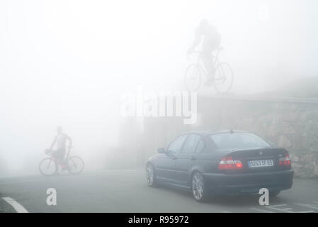 Ciclista su strada di attraversamento di fronte alla statua per il vincitore del Tour de France, Octave Lapize al Col du Tourmalet nella fitta nebbia nei Pirenei, Francia Foto Stock