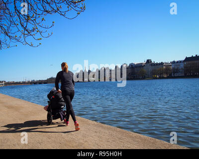 Giovane madre con un passeggino a fare jogging lungo il fiume in una città Foto Stock