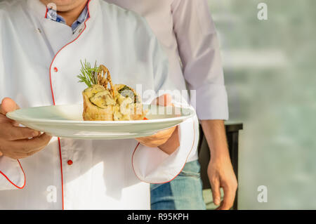 Chef in uniforme che porta una piastra con impacco con spinaci, funghi e formaggio fuso e cracker Foto Stock