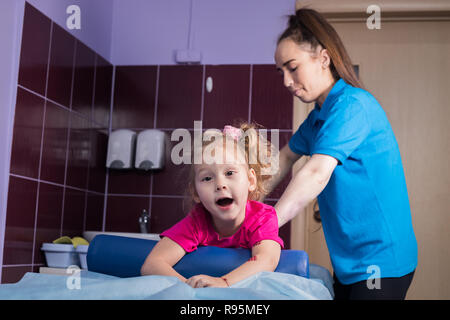 Fisioterapia con bambino con paralisi cerebrale. Una bambina in clinica giace sul lettino Foto Stock