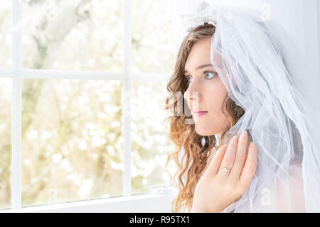 Lato Closeup, profilo Ritratto di giovane persona di sesso femminile, donna e sposa abito da sposa, velo, viso, collana di perle, capelli in piedi, guardando attraverso il vetro Foto Stock