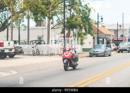 Key West, Stati Uniti d'America - 1 Maggio 2018: Overseas Highway Road, US1, auto guida anteriore della donna seduta, equitazione motocicletta, rosso lancia scooter in Florida Foto Stock