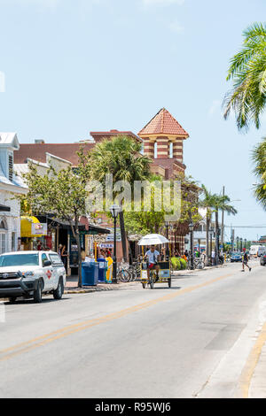 Key West, Stati Uniti d'America - 1 Maggio 2018: Duval Street road, marciapiede in Florida keys città viaggi, giornata di sole sulla strada, persone a cavallo in rickshaw, manuale a pedale taxi, Foto Stock