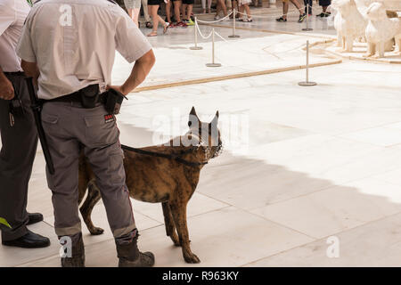 Due poliziotti in piedi all'interno di Alhambra Palace con un cane da guardia. Sullo sfondo, i turisti sono visti. Un leone bianco architettura sagomata è visibile anche su Foto Stock