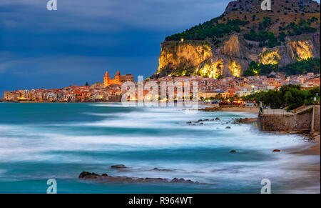 Ora blu scena di Cefalu town, con sfocata della superficie del mare e montagna illuminato in Sicilia Isola, Italia Foto Stock