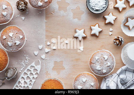 Vista superiore della tavola di legno con zucchero-spruzzata muffin, ghiaccio fondente e la stella di Natale i cookie Foto Stock