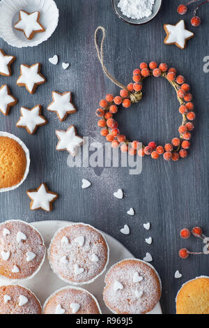 Vista superiore della tavola con zucchero-spruzzata muffin e stella di Natale i cookie e inverno decorazioni su scuro dello sfondo testurizzata Foto Stock