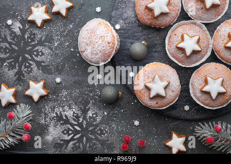 Vista superiore della tavola con zucchero-spruzzata muffin e stella di Natale i cookie su scuro dello sfondo testurizzata Foto Stock