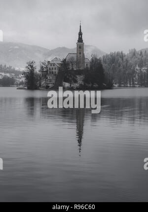 Foto del Pellegrinaggio chiesa dell Assunzione di Maria su di un isola del lago di Bled, Slovenia. Snowy cattura, in scala di grigi artistico umore Foto Stock