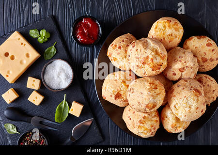 Gougeres, formaggio bignè palle su una piastra nera. Tradizionale formaggio francese choux ciambelle. formaggio e salsa di pomodoro su tavoli in legno nero, vista da sopra, Foto Stock