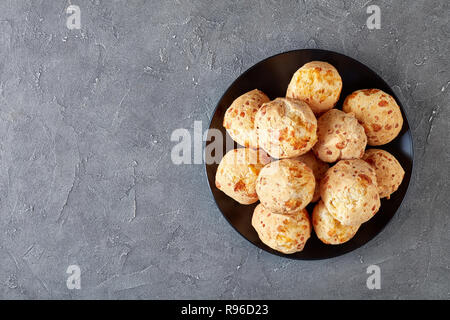 Vista aerea del Gougeres, formaggio bignè palle su una piastra nera. Tradizionale formaggio francese choux i panini su una tavola di cemento, vista da sopra, flatlay, cl Foto Stock