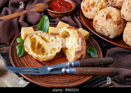 Close-up di Gougeres, formaggio bignè sfere tagliati a metà su un piatto di terracotta. classico formaggio francese choux ciambelle. panno marrone, formaggio e salsa di pomodoro Foto Stock