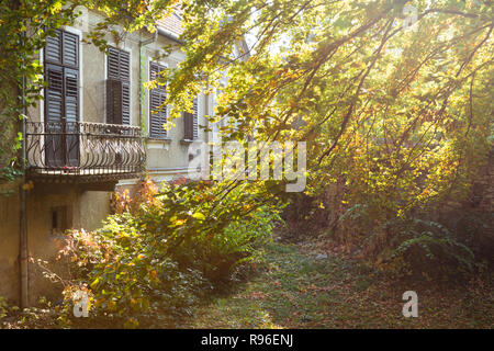 Vecchia casa del balcone e giardino frontale in autunno / caduta. Le finestre sono coperte con otturatore-persiane Foto Stock