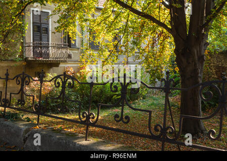 Vecchia casa del balcone e giardino frontale in autunno / caduta. Le finestre sono coperte con otturatore-persiane Foto Stock