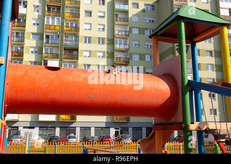 Bambino al parco giochi fa capolino fuori dal foro di un grosso arancio tubo giocattolo. Foto Stock