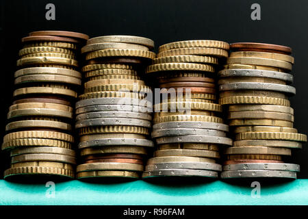 Quattro pile di monete in euro sul turchese del notebook su sfondo nero. Per argomenti economia, bilancio familiare, risparmi Foto Stock