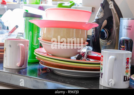 Lastre, piatti e tazze impilate su un piano di lavoro di una cucina pronta per essere lavata. Foto Stock