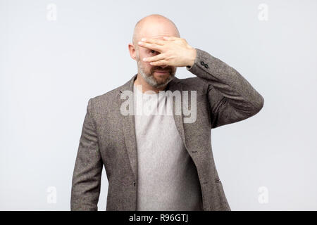 Unione uomo maturo che copre il volto con la mano e fa capolino in telecamera Foto Stock