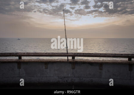 Canna da pesca sul peer in legno al tramonto in spiaggia Foto Stock