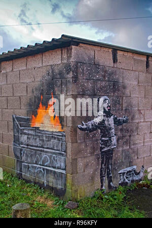 Port Talbot, Wales, Regno Unito. 19 dicembre 2018. Nuovi graffiti in Port Talbot da anonimo artista di strada Banksy. L'illustrazione mostra un bambino con le braccia aperte in riproduzione in ciò che sembra essere la neve con una slitta al suo fianco, ma l'altro lato della parete rivela è una cenere da un cestino della spazzatura sul fuoco. Credito: Phil Rees/Alamy Live News Foto Stock