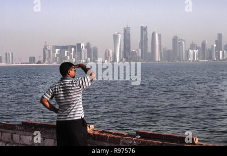 13.09.2010, Doha, Qatar - un uomo è in piedi al mare lungo la Corniche, guardando lo skyline della città del Central Business District. Foto Stock