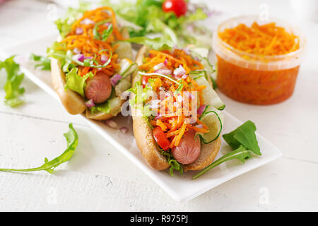 Hot Dog con il cetriolo, la carota, pomodori e lattuga su sfondo di legno. Il fast food menu. Foto Stock