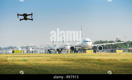 Drone senza pilota battenti vicino alla fila di aerei commerciali in aeroporto, interruzione dei voli concetto - composito digitale Foto Stock