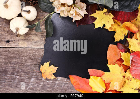 Blank chalk board circondato da foglie di autunno, fiori e zucche bianco su un sfondo rustico. Foto Stock