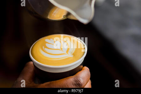 Caffè africani Barista versando una foglia forma con schiuma di latte in un take away cup Foto Stock