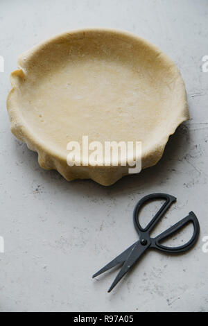 Materie non cotti base di pastafrolla per torta in teglia con le forbici su sfondo di calcestruzzo Foto Stock